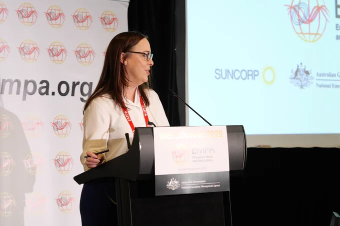 A woman in a white shirt with long brown hair speaks in to a microphone. 