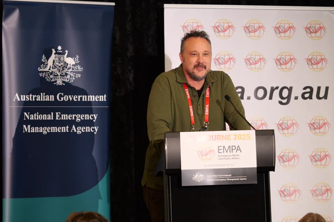 Man in khaki green shirt speaks at a podium, smiling. 
