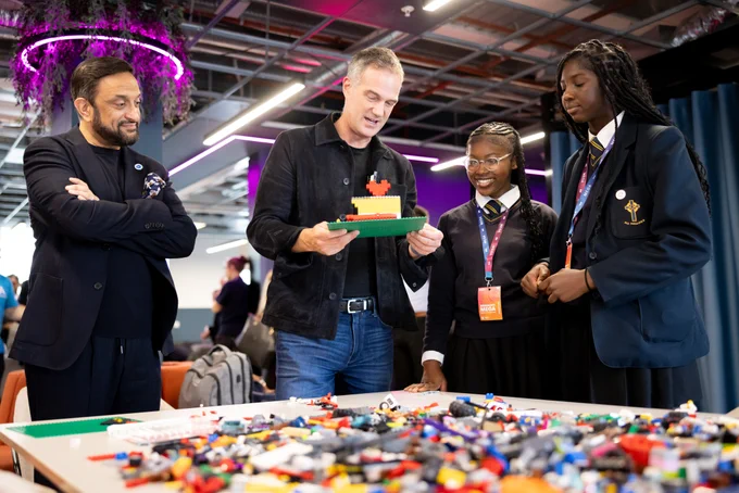 From left to right: Mo Isap, CEO for In4Group, and Science Secretary, Peter Kyle, speak with two female students, while holding a LEGO model they've created. 