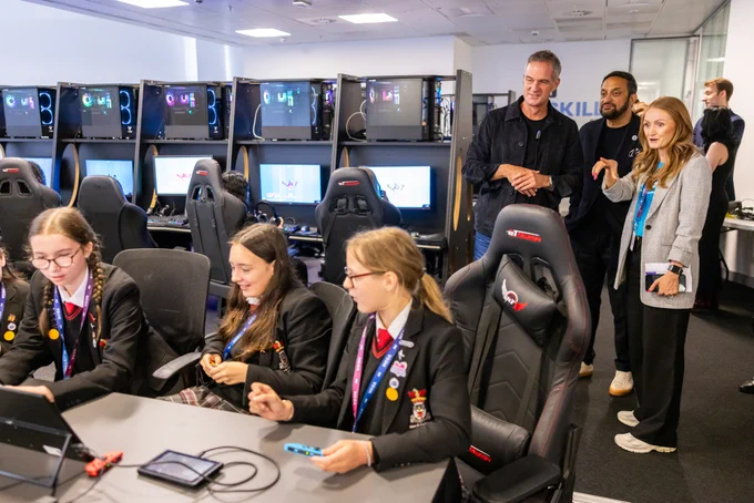 Left-hand side show three girls sitting at computers, completing a task. Standing behind them is Science Secretary, Peter Kyle, Mo Isap, CEO for In4Group, and Lauren Monks, Director of Strategy for In4Group, who is explaining the activity. 