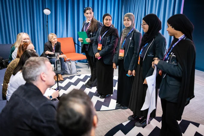Bottom left-hand corner shows Science Secretary, Peter Kyle and Mo Isap, CEO for In4Group, listen to five secondary school girls as they talk through their product prototype presentation. 