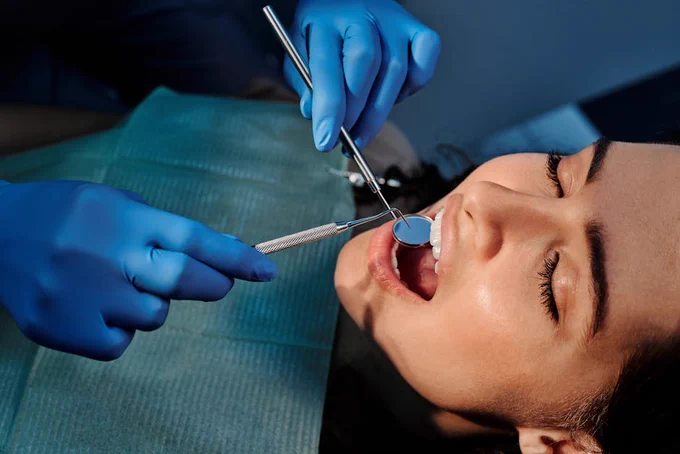 A person receiving dental services, the dentist has gloves on and is inspecting the person's mouth.