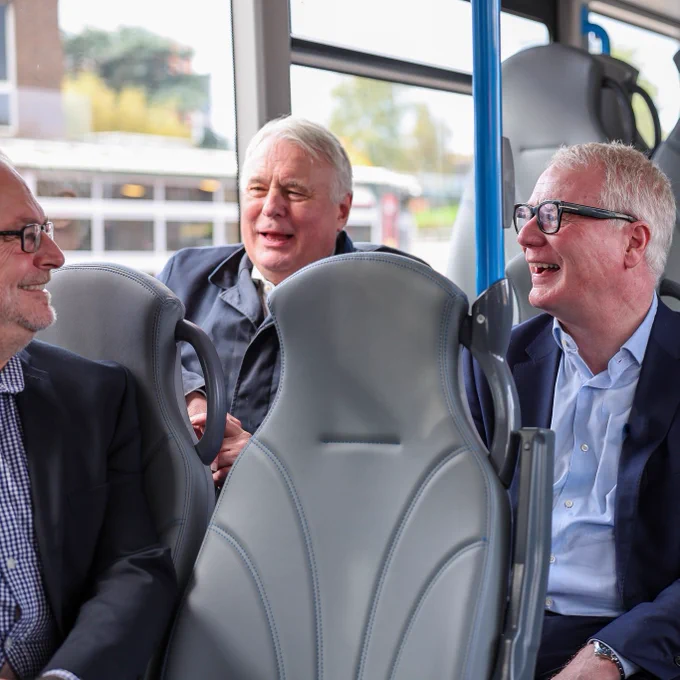 Photograph of three men sat chatting on an electric bus. 