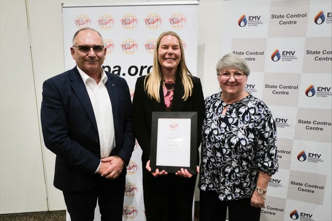 A woman stands in between two people holding a framed certificate.