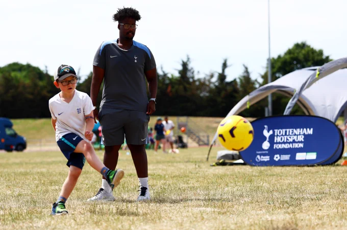 A young participant kicks a football while a Spurs Foundation coach cheers them on during Great Ormond Street Hospital’s Sports Day.