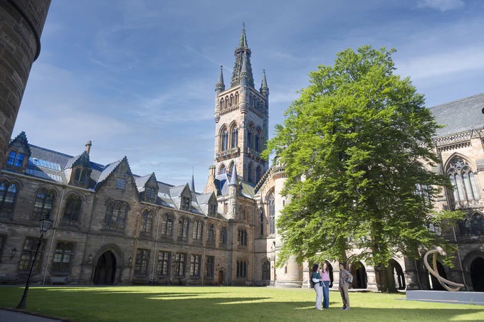 Three students standing in the University quadrangle. The tower and historic main building is in the background.
