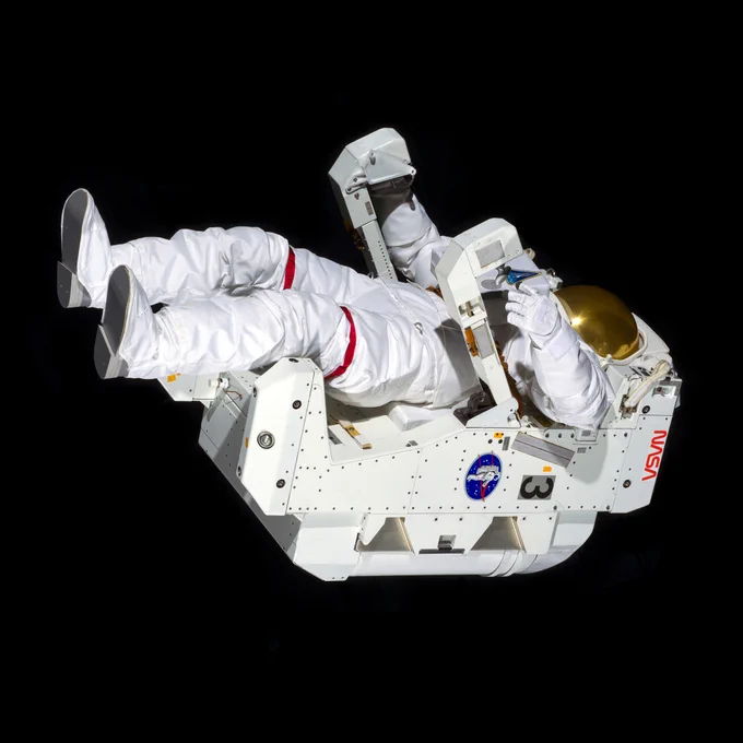An mannequin wearing in a white space suit with a gold visor, attached to a NASA Manned Maneuvering Unit, photographed as if floating in space.