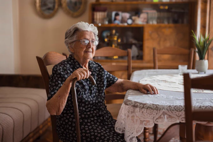 An elderly lady sitting in her home at the kitchen table smiling. 