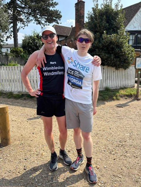 Georgia, a Share student, standing next to her running buddy, with one arm around him. They are both wearing running shirts and shorts.