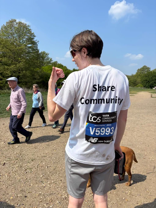 Georgia, a Share student, showing off the back of her running t-shirt. There is a TCS label with her marathon number and text on the shirt that reads: Share Community