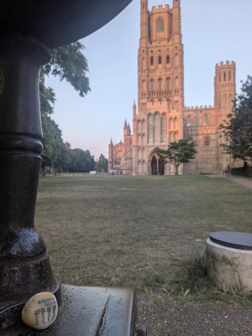 Stone photographed across the grass from  the front of a cathedral in evening sunlight