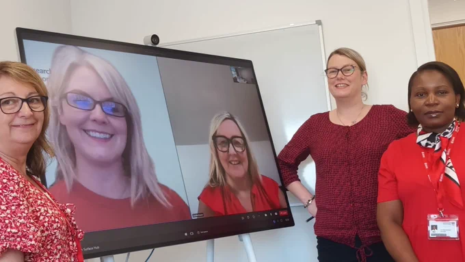 Two people on a screen next to three people. All are wearing red clothing. 