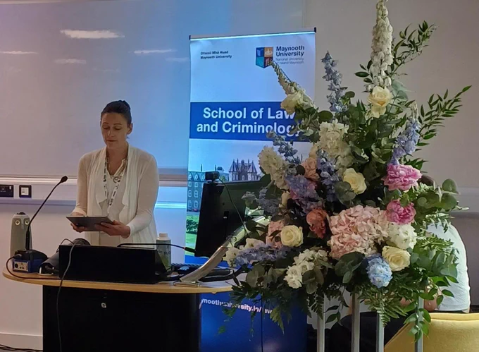 Photo of Dr. Irvinepresenting from a podium with a flower display to the side.