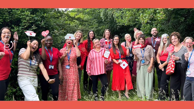 Group of staff wearing red for research. Holding red cardboard props including glasses and hats.
