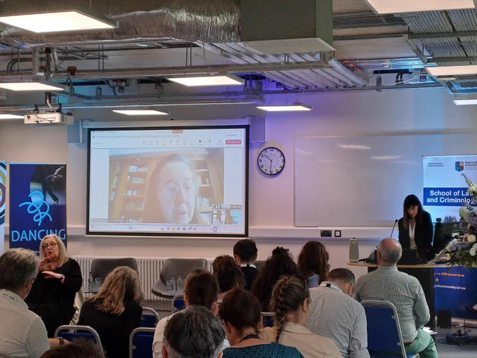 Photo of the speaker presenting on a large screen at the conference.