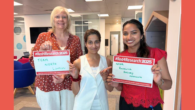 Three members of staff wearing red for research and smiling in the office.