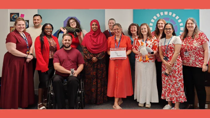 Large group of staff wearing red for research. Sign reads 'we love research'.