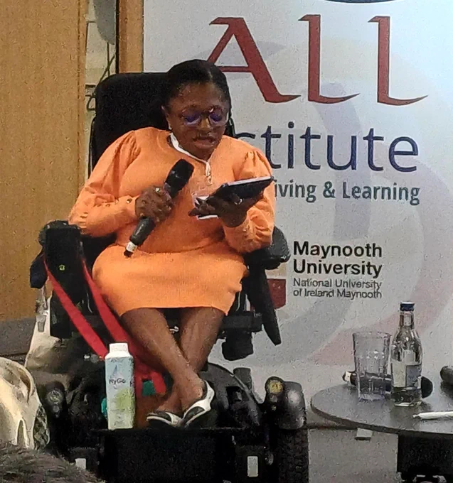 Photo of Monique Dior Jarrett of Stopgap presenting into a microphone with the backdrop of the ALL INstitute banner behind.