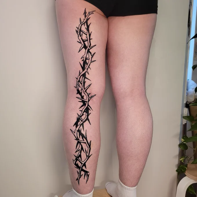 giant blackwork tattoo by spoopy. features 2 interwoven thorns going down the back of somebody's entire leg.