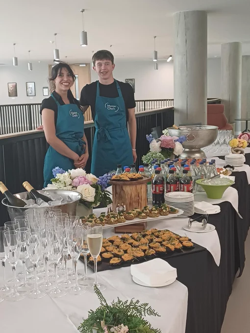 Photo of Masterchefs staff standing in front of a table with wine glasses and canapes.
