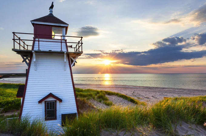 Lighthouse in front of a sandy beach during sunset.
