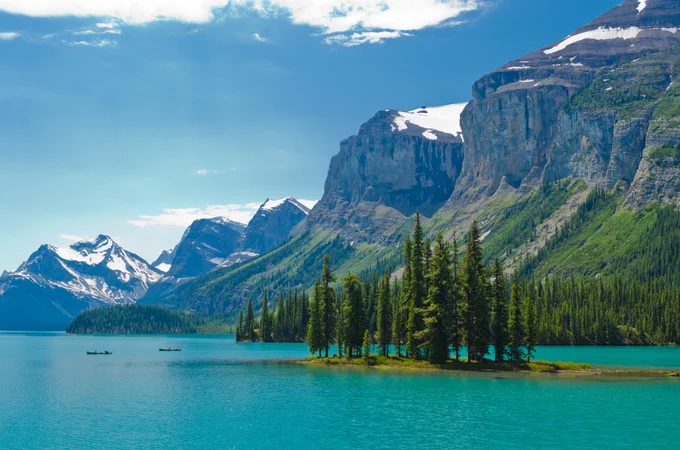 Bright blue waters sit under a range of snow-capped mountains on a sunny day.