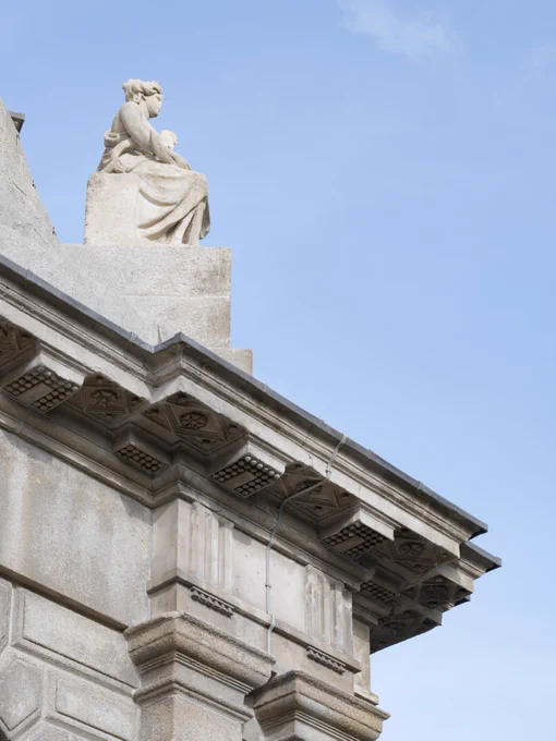 Statue sitting atop the corner of the campanile, a  stone building against a clear blue sky.