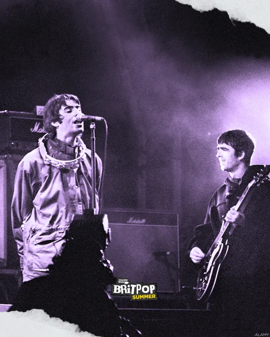A black and white archive photo of Liam Gallagher on stage in 1995. Liam is singing, Noel is playing guitar and smiling.