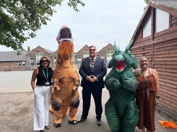 Mayor of St Helens borough, Cllr Seve Gomez-Aspron, pictured with District Primary staff and 2 people in inflatable dinosaur costumes