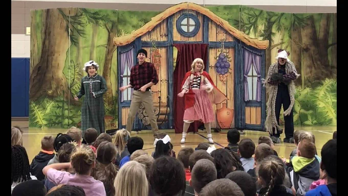 Four actors dressed as fairy tale characters perform on stage in front of an audience of children.
