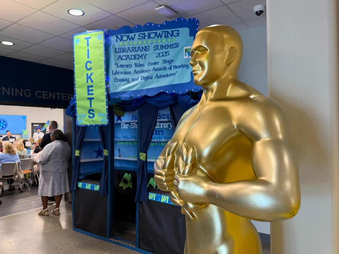 A statue stands in front of a sign for the Librarians Summer Academy.