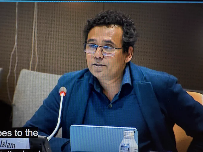 Man with black curly hair and glasses and wearing blue shirt and suit jacket speaking into a microphone at the United Nations Side Event