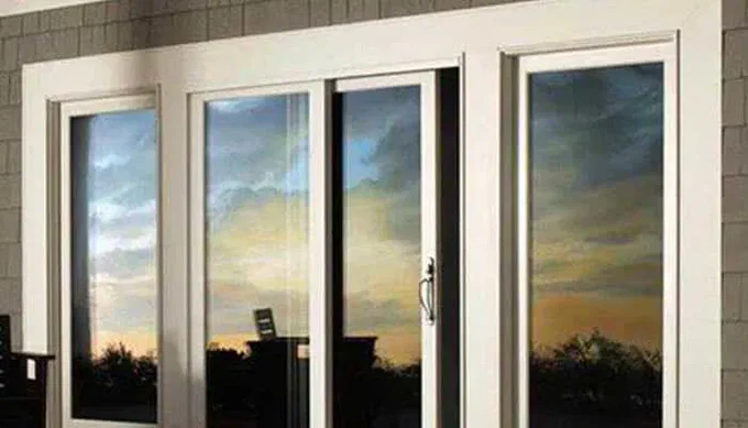 A row of white-framed impact rated windows reflecting a colorful sunset sky and silhouetted outdoor landscape.