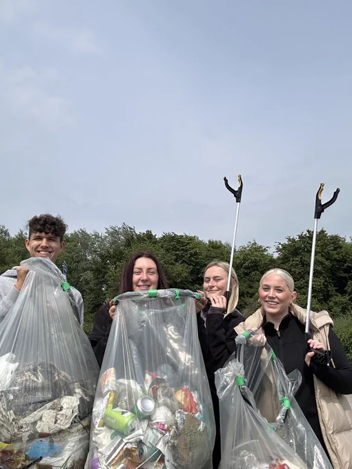 A group of four people carries trash bags, and one person is digging with a shovel, engaged in environmental cleanup.