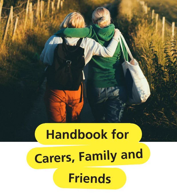 Two people walking down a path with their arms around each other. They are surrounded by tall grass and a fence on either side of the path. The text at the bottom of the image reads: "Handbook for Carers, Family and Friends".