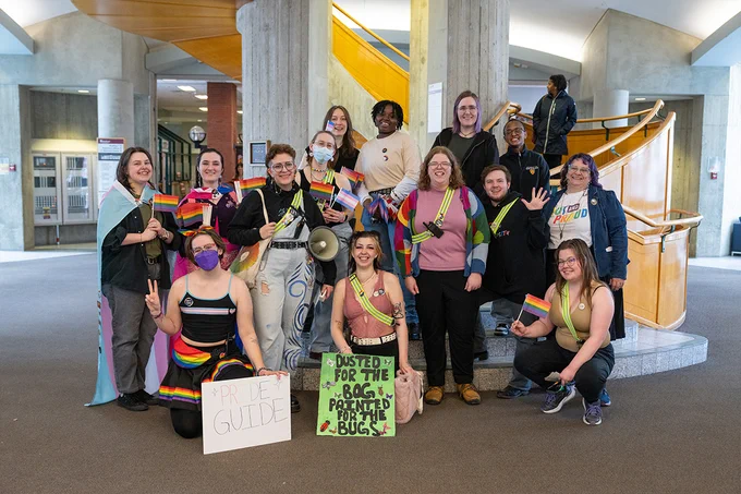 A large group of people pose for a photo in front of MacEwan's spiral staircase. 