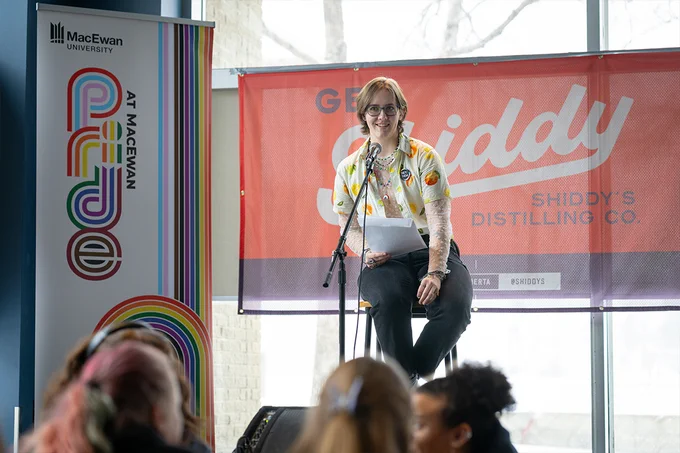 A person sitting on a stool and speaking into a microphone.