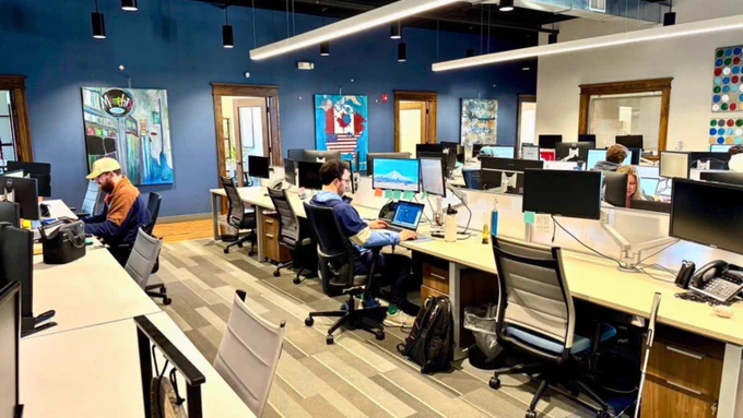 Open office space at CAT Global with employees working at multiple computer stations under modern lighting, featuring artwork and a productive environment.