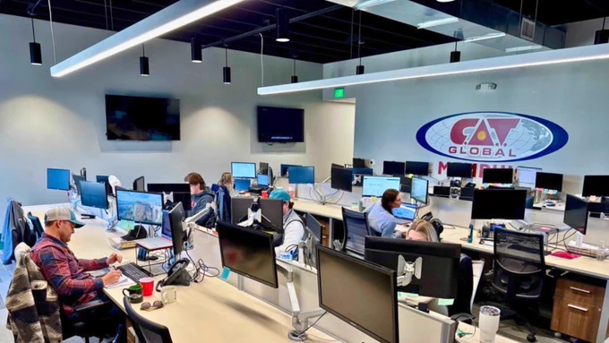 Collaborative workspace at CAT Global with employees managing logistics operations, highlighted by the large CAT Global logo on the wall.