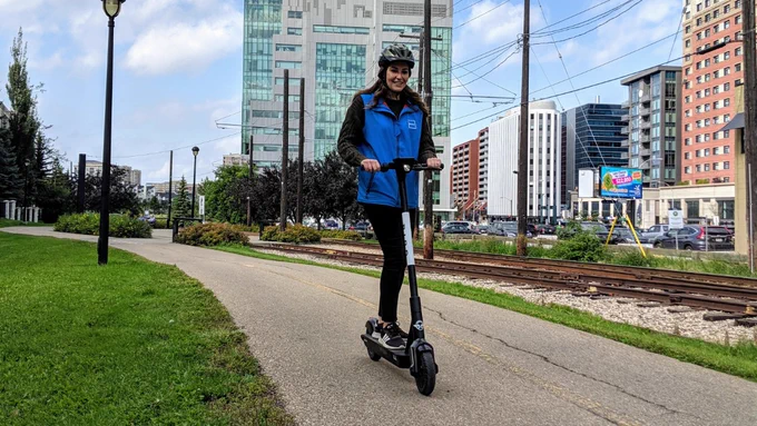 A woman wearing a helmet rides a shared e-scooter on a Shared Pathway. 