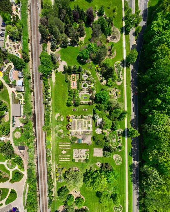 Aerial view of a garden layout surrounded by greenery, with adjacent railway and road.