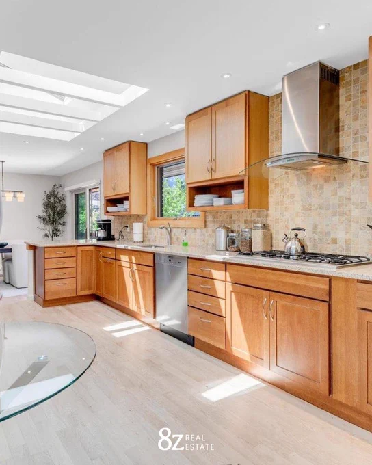 Modern kitchen interior with wooden cabinets, stainless steel appliances, and a glass dining table, showcased by 8z Real Estate.