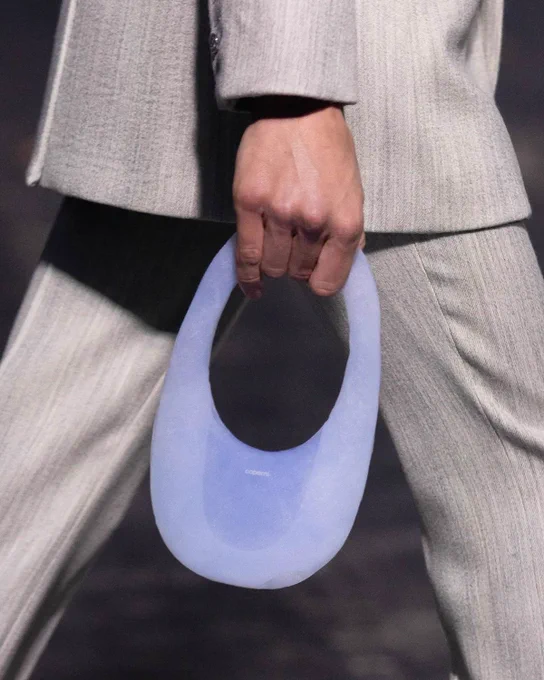 A model holds a small purse made of aerogel, with a softly transparent blue color and adorned with the logo of the Coperni fashion brand.
