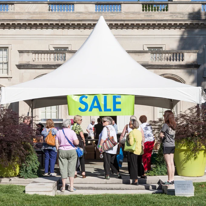 A group of shoppers gather near and under a white tent on VMFA's Pauley Center Patio. The tent displays a large sign that reads, "SALE."
