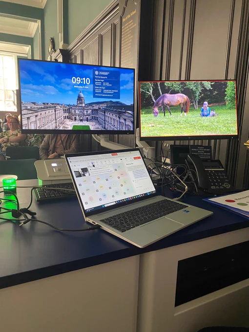 Photograph of laptop with Teams meeting and presentation playing (monitor has photograph of person sitting near a horse in a field). 