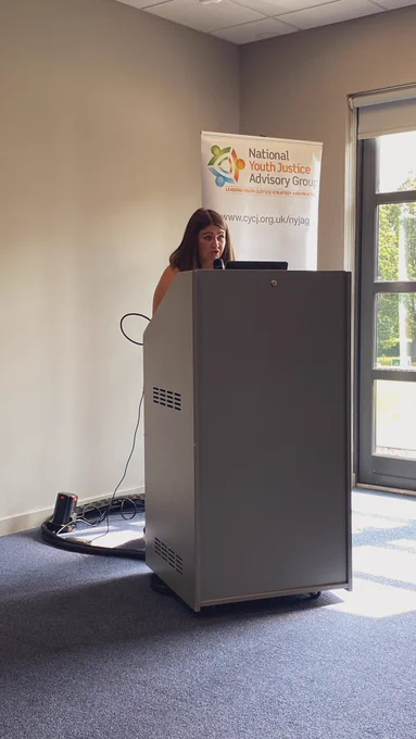 Nicole Savage standing at a lectern in front of the NYJAG banner