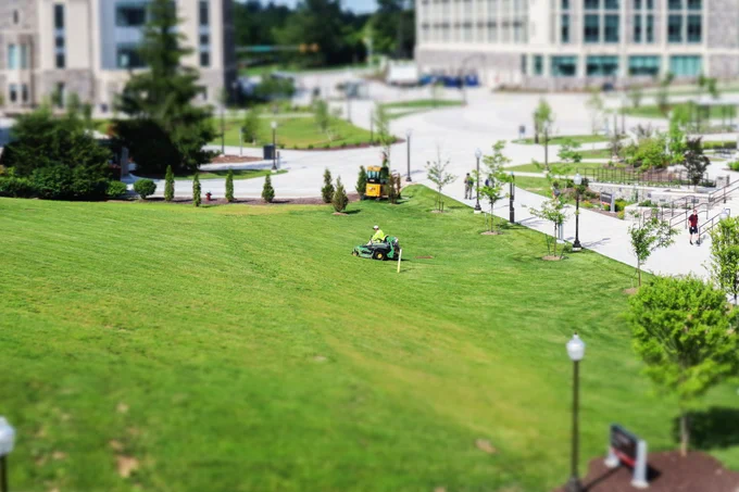 A Virginia Tech facilities member cuts the grass outside of Whittemore Hall captured with tilt shift photography.