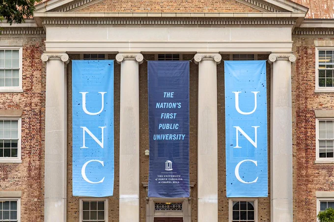 Banners on South Building on UNC's campus spell "UNC" and "The Nation's First Public University"