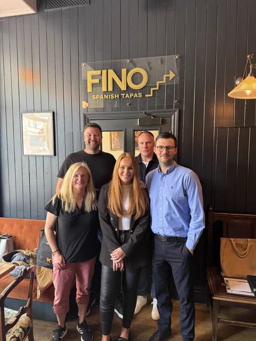 A picture of Dr Liv Williams (centre front) with her  PhD supervisors, Jess Macbeth (front left), Andy Sprake (back left), Alan Thomson (back right), and External Examiner,  Anthony Maher (front right). All five are pictured standing together in a restaurant celebrating Liv’s success.
