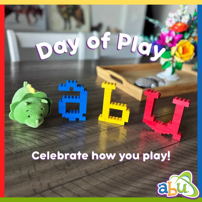 The ABU logo is built of toy bricks and sits on a table. A green stuffed triceratops sits next the "A". Text reads "Day of Play. Celebrate how you play!"
